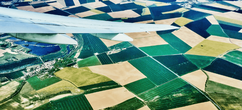 A view of an airplane wing flying over agricultural fields