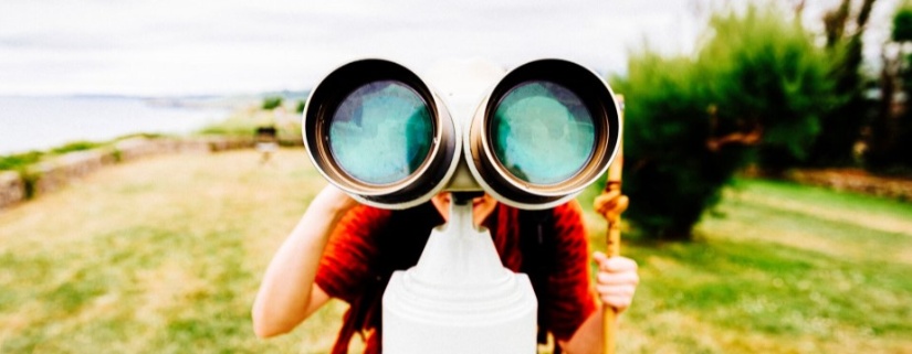 A person looks at the camera with a tower binocular at an outside viewing point