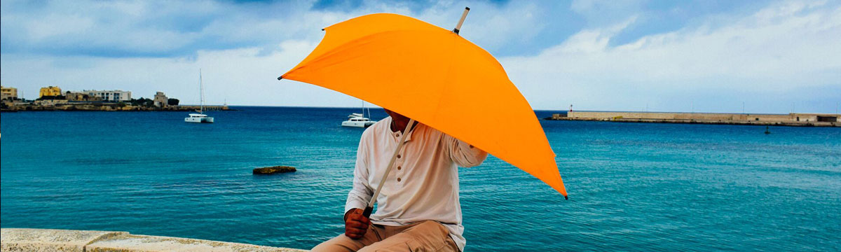 A man holding an orange umbrella by the sea